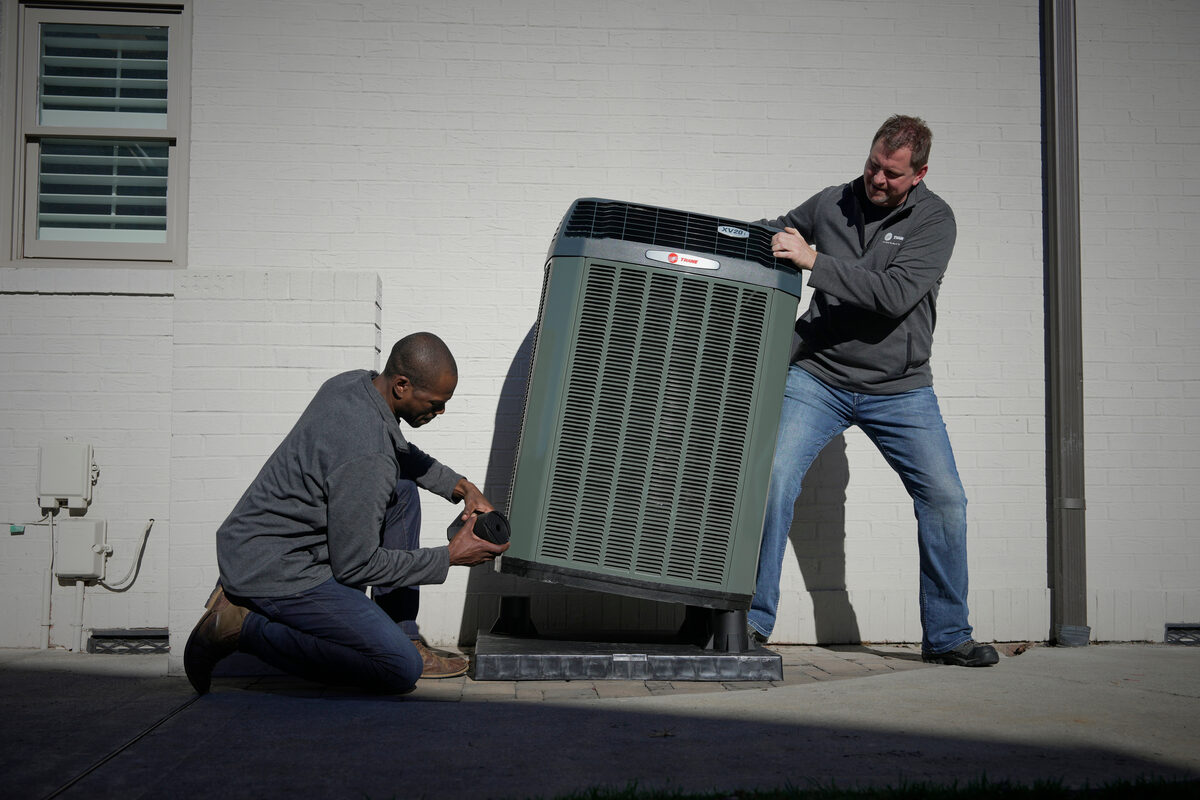 two hvac techs moving an air conditioning unit